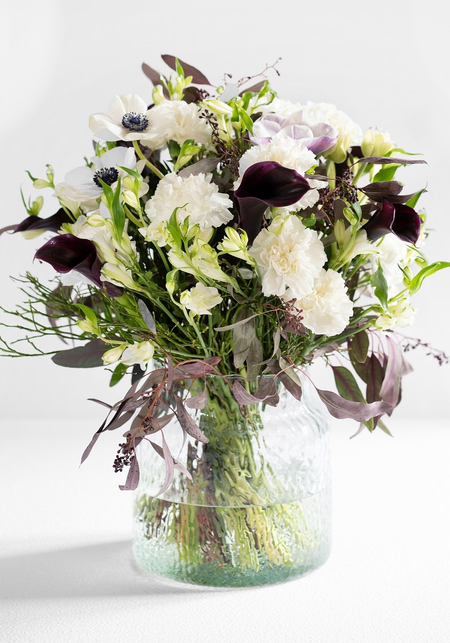 Handgebundenes Bouquet aus weißen Nelken, Anemonen und dunklen Kallas in einer Glasvase